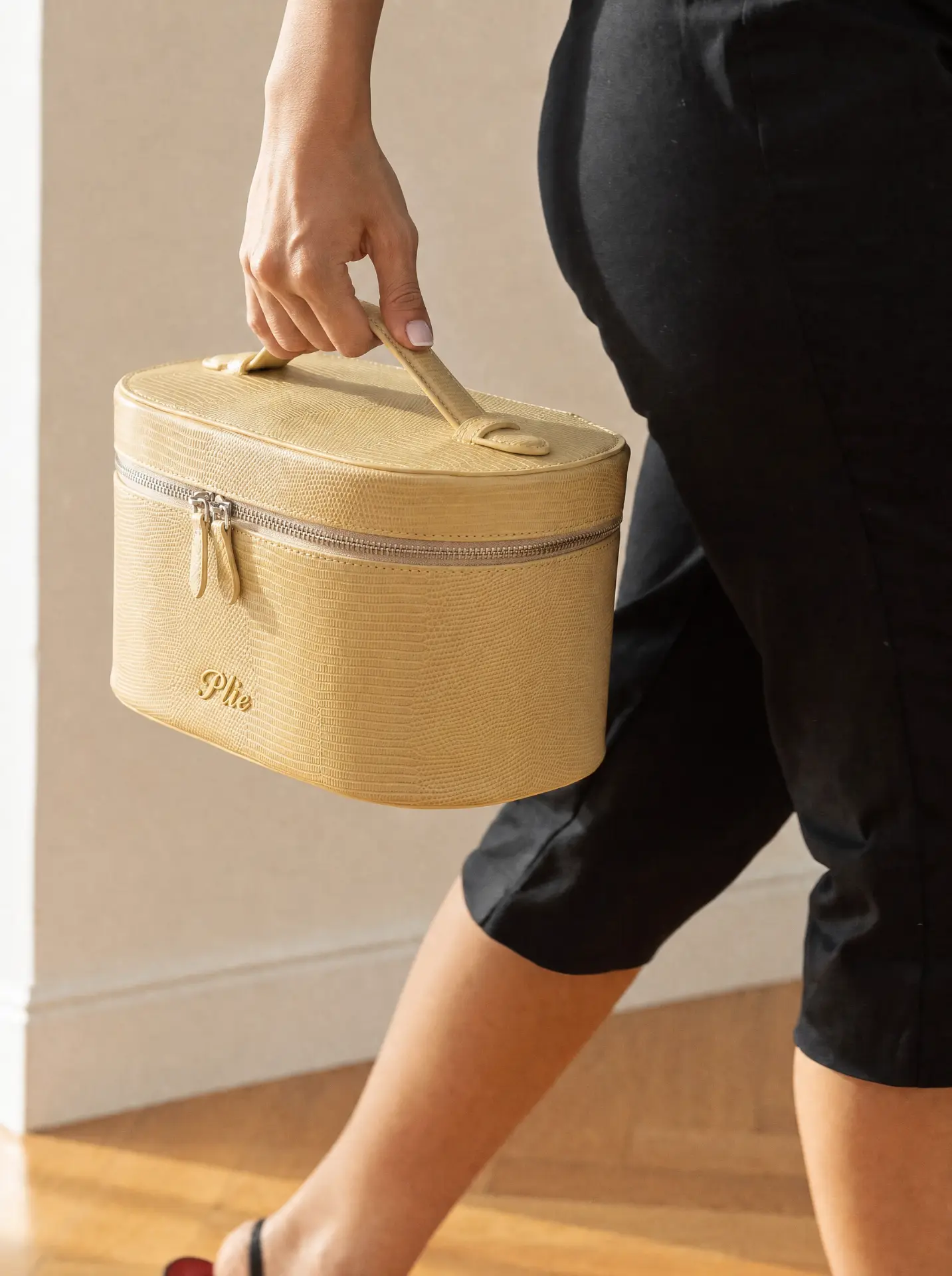 OSTIR Travel Case in butter lizard-embossed finish with Plié logo, carried in hand